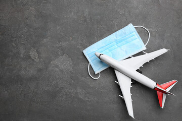 Toy airplane and protective mask on grey background, flat lay with space for text. Travelling...