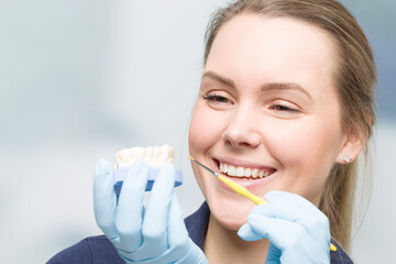 Smiling female dental technician doing painting work at artificial dentition  on dental imprint in...