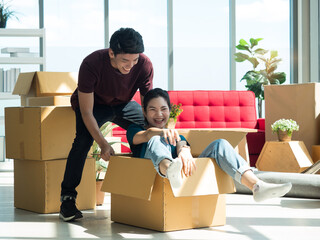 Asian young couple playing and having fun while moving or unpacking, woman in the carton box while man pulling the box.