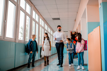 Elementary school students and male teacher wearing protective face masks at school