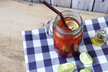 a glass of iced lemon tea with honey is put on the wooden table with background of wooden wall of the kitchen during party with happy family