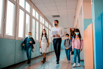 Elementary school students and male teacher wearing protective face masks at school