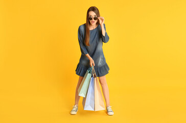 Beautiful young woman with paper shopping bags on yellow background