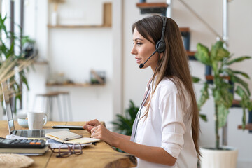 Focused businesswoman sitting on table, participates in videoconference, wear headphones, communicating with client via video computer call. Customer care service support helpline from home