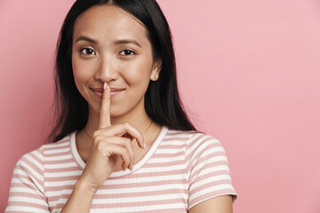 Beautiful smiling asian woman showing silence gesture at camera