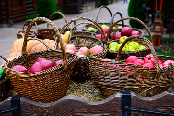 Wicker baskets with tomatoes, with red and green apples on a straw.