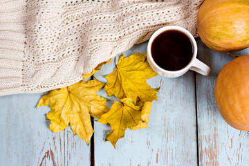 Autumnal composition with pumpkins, leaves, a blanket and coffee on light wooden boards.