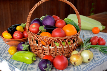 Wicker basket with fresh tomatoes, eggplant, cucumbers, peppers, zucchini,onions on a napkin