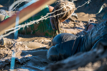 Sexy athlete crawling in mud under barbed wire at an obstacle course race