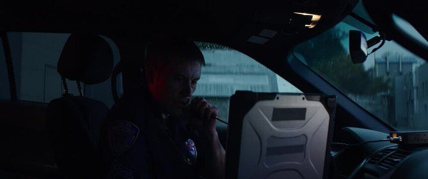 Portrait of police officer talking on CB radio while checking information on a laptop inside a car. Shot on RED Dragon with 2x Anamorphic lens