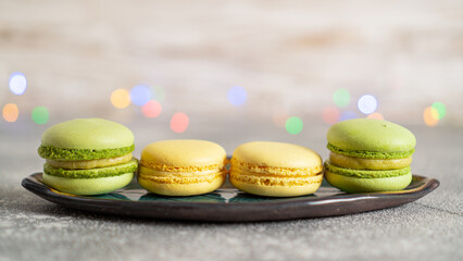Lemon and kiwi macaroon on a green plate on a colored bokeh background. Delicious cakes