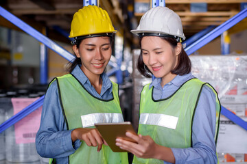 Warehouse woman wearing a hardhat standing cargo at goods or merchandise warehouse and check for control loading from Cargo freight ship for import and export by report on tablet. Teamwork concept