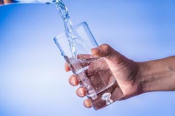 Filling up the glass with water, hand holding glass against bright blue background
