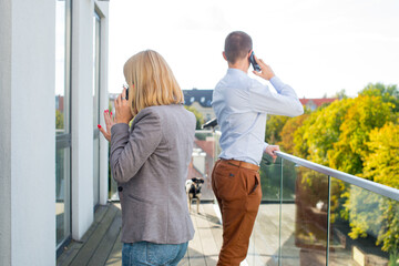 The woman and the man on the terrace are talking on the phone separately. Businesswoman and businessman with mobile phone on terrace. Work from smartphone. Covid theme. Pandemic theme.