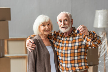 senior man embracing wife and holding keys, moving concept