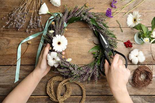 Florist making beautiful autumnal wreath with heather flowers at wooden table, top view