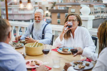 Senior multiracial people having fun at patio dinner - Happy friends eating at sunday meal - Focus on hipster man face