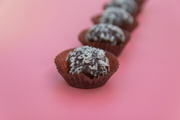 Coconut petit four is a juicy chocolate sponge cake with coconut filling and topping with coconut flakes. Mini cake on a pink background. Selective focus.