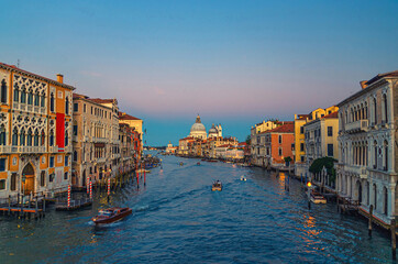 Fototapeta premium Venice cityscape with Grand Canal waterway. Buildings with evening lights along Grand Canal. Santa Maria della Salute Roman Catholic church on Punta della Dogana at twilight. Veneto Region, Italy.