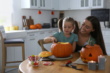 Mother and daughter making pumpkin jack o'lantern at table in kitchen. Halloween celebration