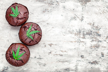 Chocolate cupcake muffins with cannabis leaves weed cbd. Medical marijuana hemp drugs in food dessert. Cooking baking weed muffins with marijuana on gray concrete background. Copy space. Top view.