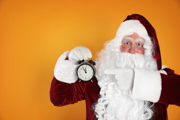 Santa Claus holding alarm clock on yellow background, space for text. Christmas countdown