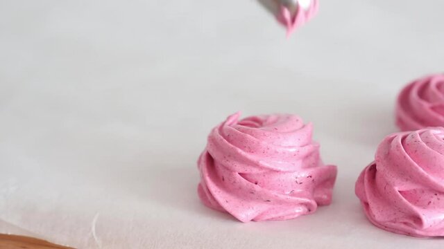 Squeezing pink cream out of a baking bag to make dessert