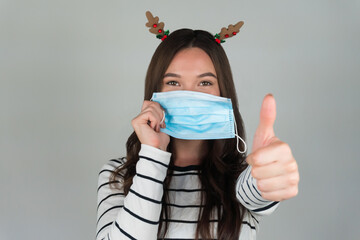 Beautiful young brunette with a medical protective mask on a gray background. A woman poses with a...