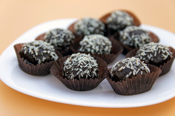 Coconut petit four is a juicy chocolate sponge cake with coconut filling and topping with coconut flakes. Mini cake in a white plate. Selective focus. Place for text.