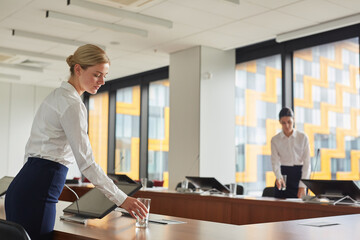 Portrait of female assistant putting glass of water on table while preparing conference room for business event, copy space