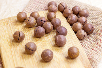 Brown macadamia nuts with wooden cutting board on light textile background.
