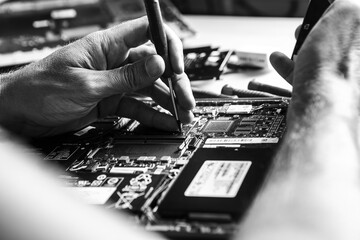 The laptop is located on the desktop. The computer service technician opens the lid with a screwdriver because he wants to install new components in it. Black and white.