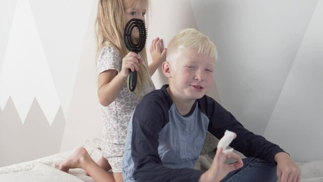 The little sister combs the hair of the elder's blond hair.