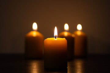 Group of lit candles burning in the darkness in golden tones with selective focus on candle and background blur