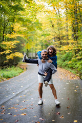 Middle aged couple piggy bag on a rural road during fall expressing excitement