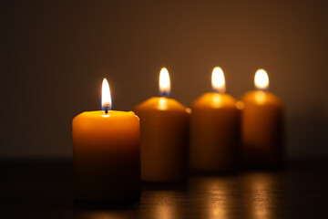 Row of lit candles burning in the darkness. Golden tones with selective focus on candle and background blur