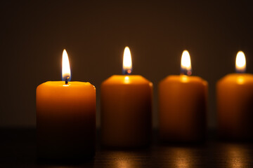 Group of lit candles in a row burning in the darkness. Golden tones with selective focus on candle and background blur