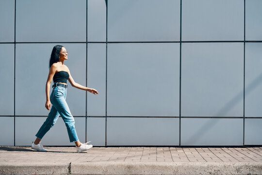 Fashionable trendy african american woman walking along street wall urban background