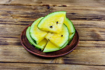 Plate with sliced yellow watermelon on a wooden table