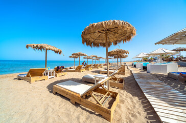 Orginized sandy beach during summer time, with wooden sun beds and straw umbrellas 