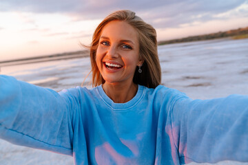 Fototapeta premium Young happy woman smiling at camera while taking selfie outdoors