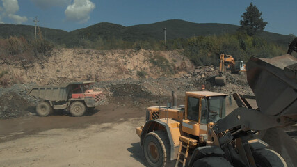 Closeup view of bulldozer. Big heaps of stones and sand. Truck is standing on the wet ground.