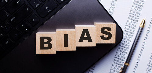 The word BIAS is written on wooden cubes on the keyboard next to the pen.