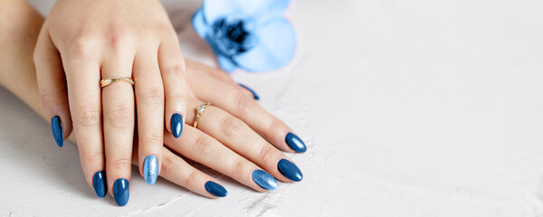 Belles mains avec manucure bleue classique à la mode allongée sur une pierre blanche