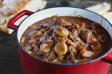 Beef Bourguignon cooked in an enameled cast iron Dutch oven and served with homemade artisan bread over a rustic wood background.