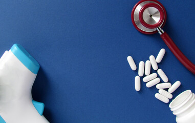 Red stethoscope, white pills and non-contact thermometer isolated on blue background. Medicine...