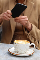 A woman using mobile phone to take a photo of coffee in Cafe