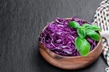 Sliced red cabbage in wooden bowl on black stone background