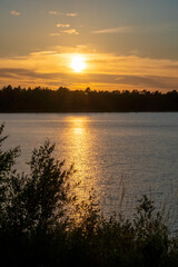 Panorama of a gorgeous sunset at a forest lake, with gold and blue color in the sky and trees reflected in the water. High quality photo