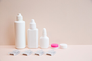 Contact lenses, lens solution and lens containers on a light pink background. Health care concept